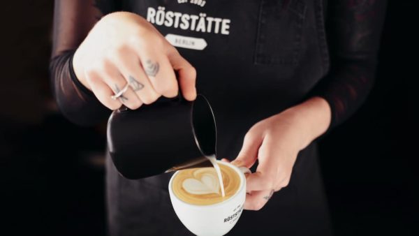 Latte Art Barista Schulung: Milchkaffee erhält Milch aus Kännchen.